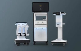 From left to right, a white platform on wheels with three robotic arms, a monitor on a white stand and another white and black stand.