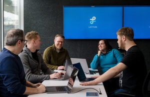 Five people sitting at a table with computers, four men and one woman, with a blue screen in the background and the Latitude AI logo.