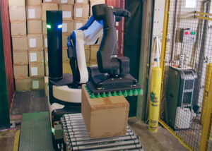 Boston Dynamics' Stretch robot using its suction gripper to drop a package onto a conveyor belt.